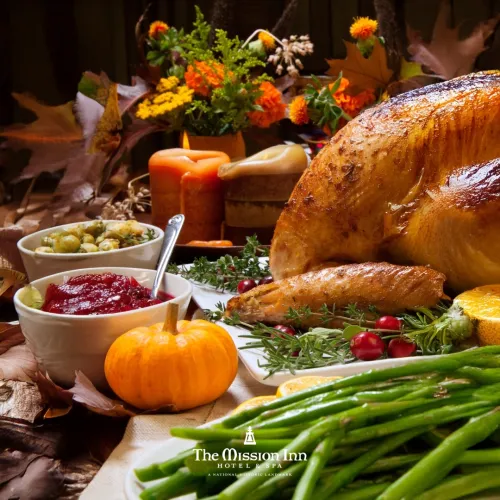 A festive autumn table with a roasted turkey, green beans, veggies, candles, and colorful floral centerpiece for a holiday feast.