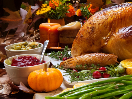 Roasted turkey and seasonal sides on a fall table with candles, pumpkins, cranberries, and fresh herbs.