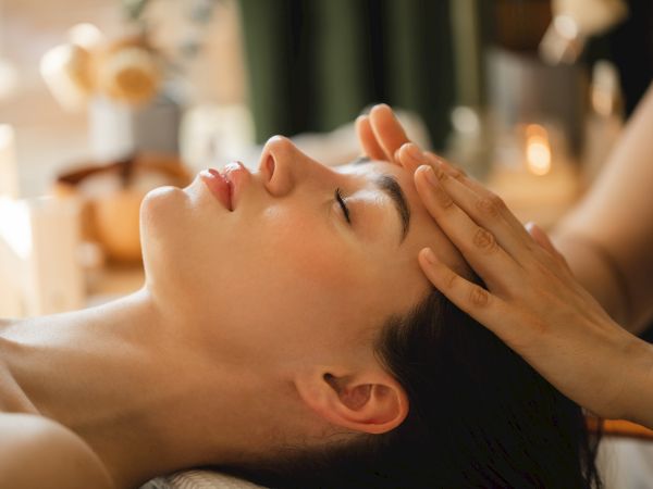 A therapist gives a relaxing face massage with hands, while the person lies down in a spa setting.