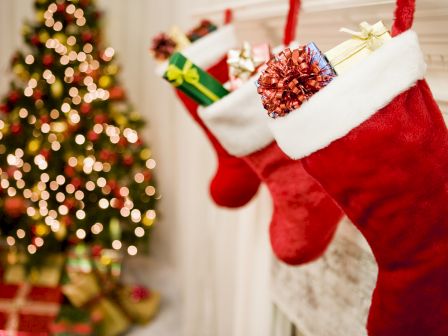 Santa&rsquo;s red-and-white stocking with a gold ribbon gift sits beside a decorated Christmas tree with lights.