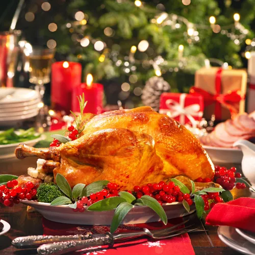 Holiday feast spread: roasted chicken on a platter, red candles, fresh herbs and cranberries, with bokeh lights in the background.