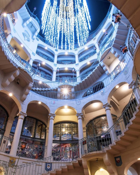 Inside a grand circular atrium with curved balconies and a domed ceiling, glowing with blue-white hanging lights and warm lamps.