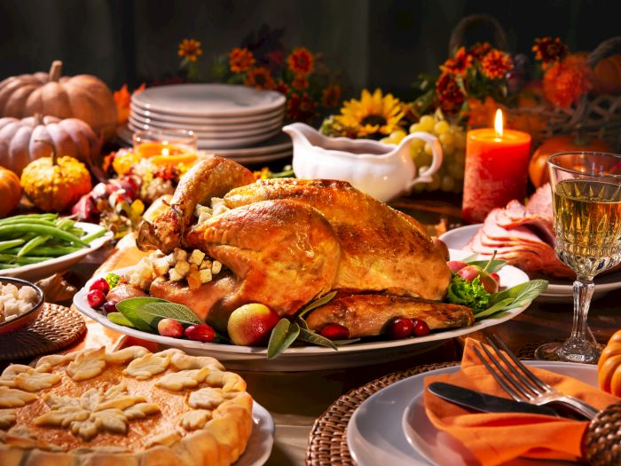 A festive Thanksgiving table with roasted turkey, pumpkins, fall flowers, candles, and wine glasses for a hearty holiday feast.