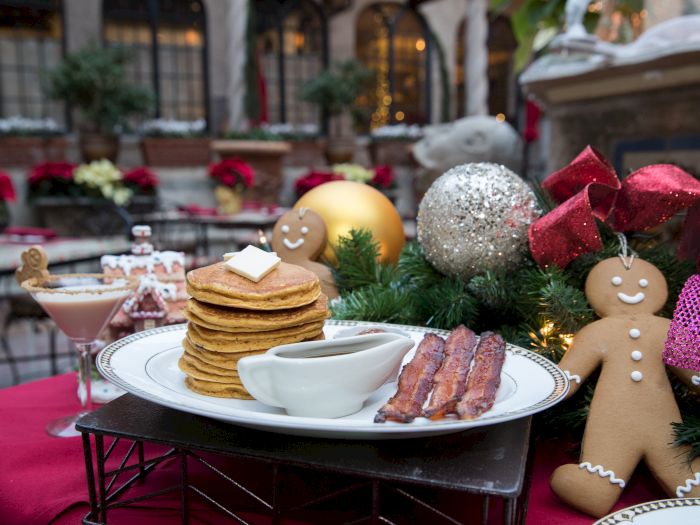 A festive holiday table with a pancake stack, bacon, and gingerbread men beside pine garland and ornaments.