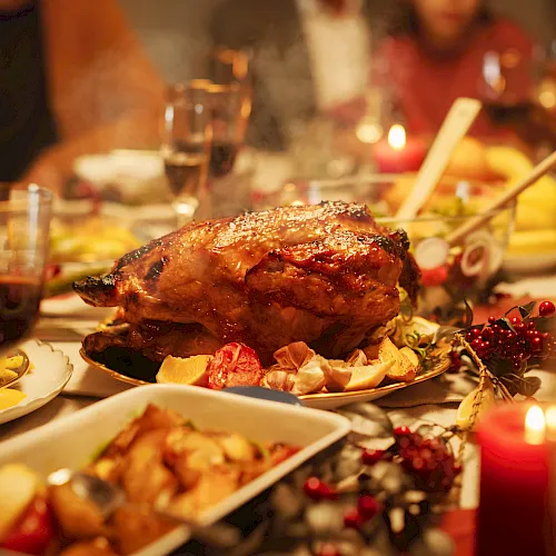 A festive dinner table with a roasted chicken on a platter, champagne flutes, and candlelit warm lights.