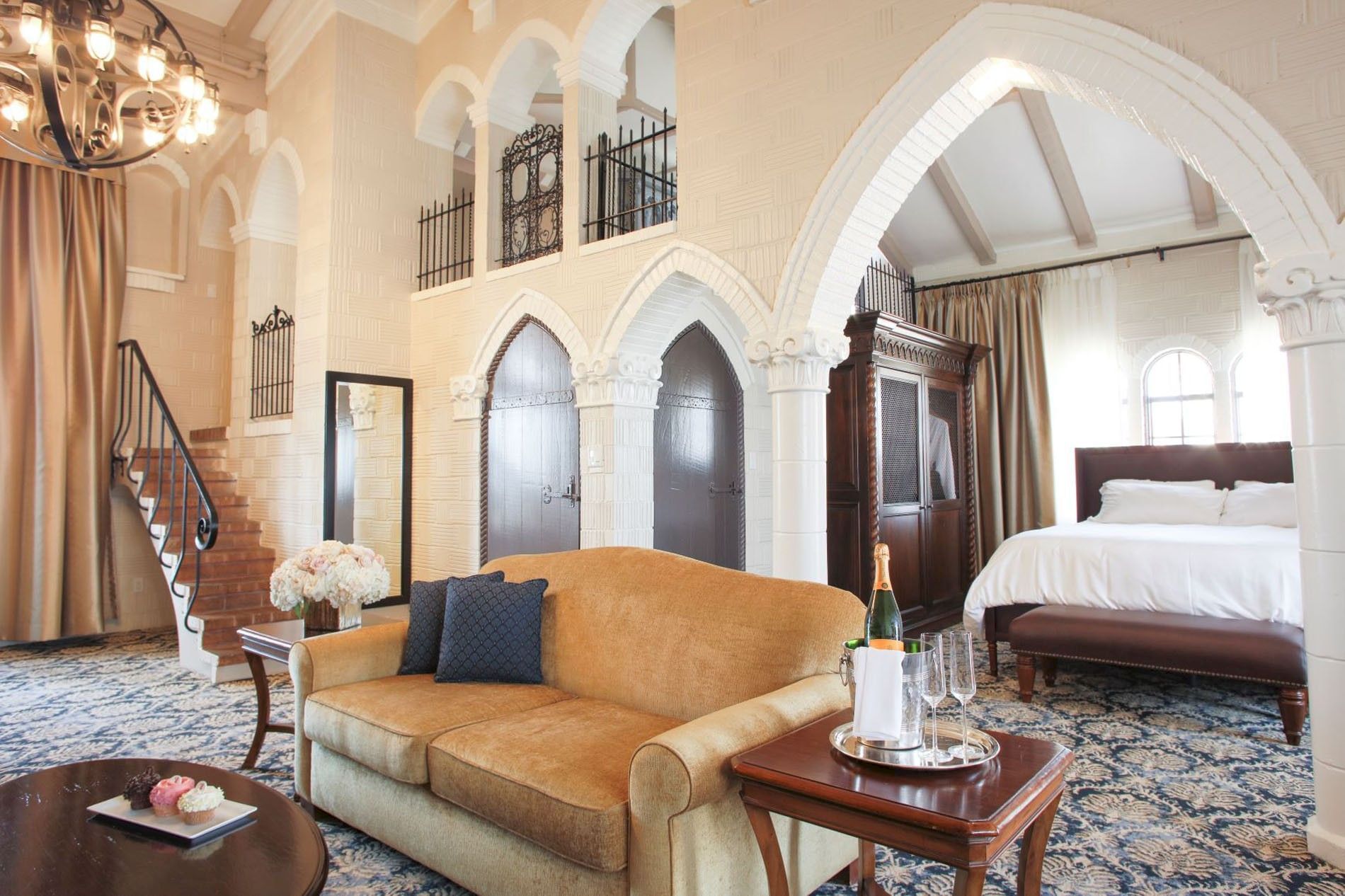 A luxurious hotel suite interior with an arched white ceiling, couch, coffee table, sparkling drinks, and a grand bed.