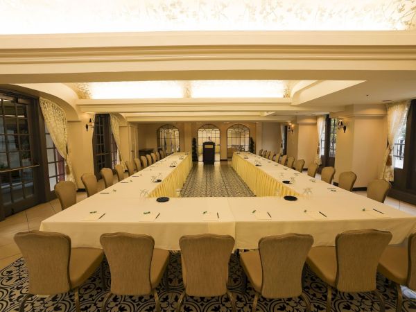 A formal banquet meeting room with long tables set with chairs, glass windows, and warm ambient lighting.