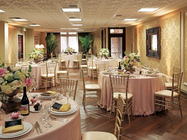 Elegant banquet hall set with round tables, gold chairs, white linens, flowers, candles, and glassware for a wedding or special event.