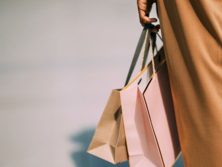 A person&rsquo;s arm with bangles holds multiple shopping bags against a soft background.