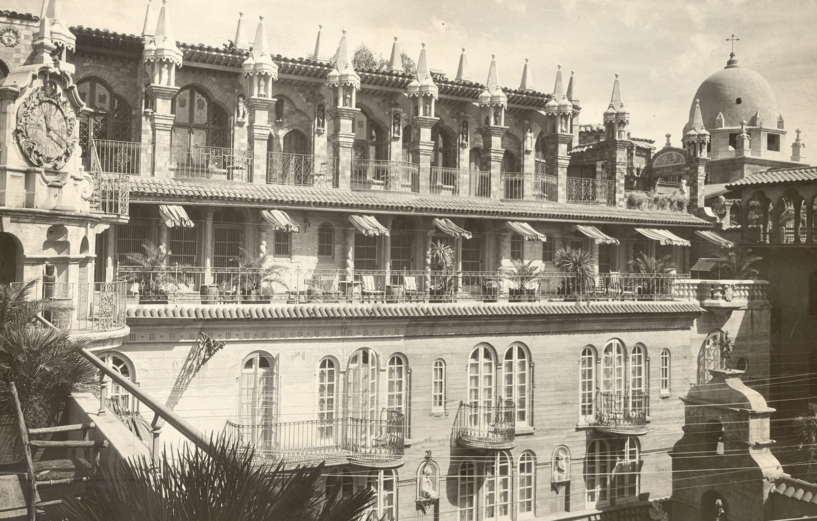 A vintage view shows an ornate stone palace with many archways, rooftop spires, and a large dome under bright sky.