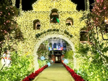 A Christmas-lit walkway with glowing trees and a decorated hotel entrance in the distance.