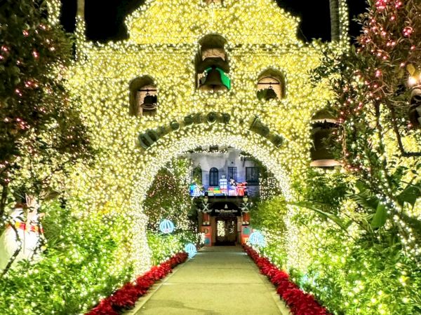 A Christmas-lit walkway with glowing trees and a decorated hotel entrance in the distance.