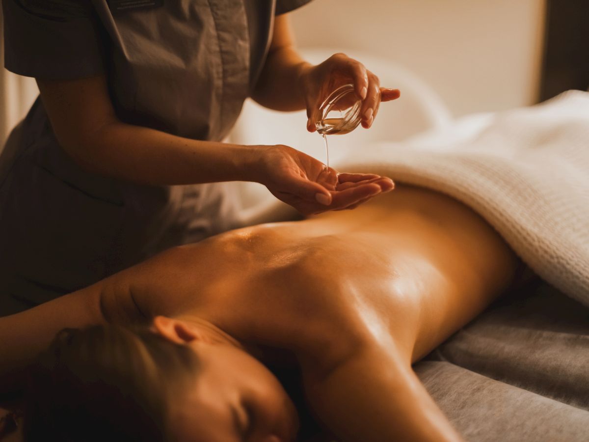 A masseur drips massage oil into their hands while preparing to give a soothing massage on a bed.
