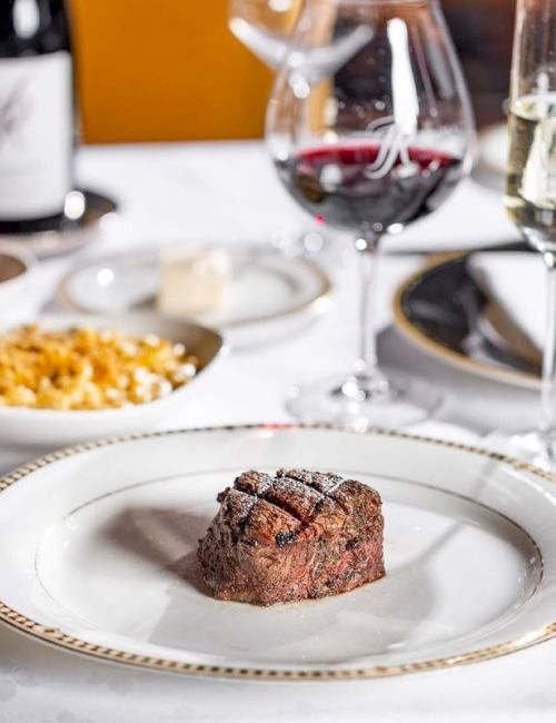 A fancy restaurant table set with plated dinner, wine glasses, and a chocolate dessert in the foreground, ready to serve.