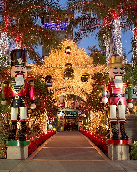 A festive garden walkway lit with sparkling strings, featuring large nutcracker soldiers and a castle-like display in the background.
