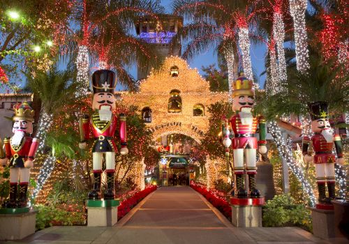 A festive garden walkway lit with sparkling strings, featuring large nutcracker soldiers and a castle-like display in the background.