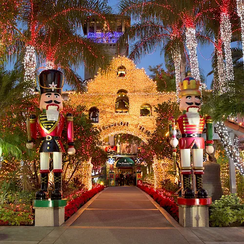 A festive garden walkway lit with sparkling strings, featuring large nutcracker soldiers and a castle-like display in the background.