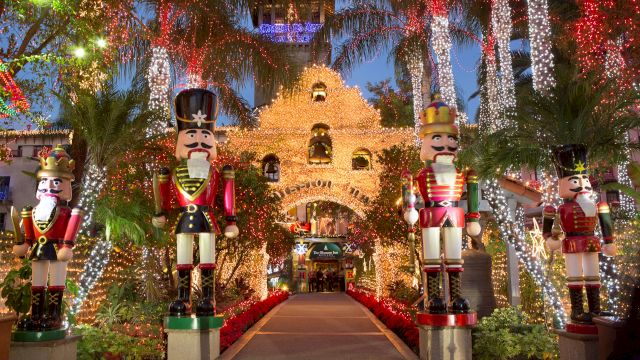 A festive garden walkway lit with sparkling strings, featuring large nutcracker soldiers and a castle-like display in the background.