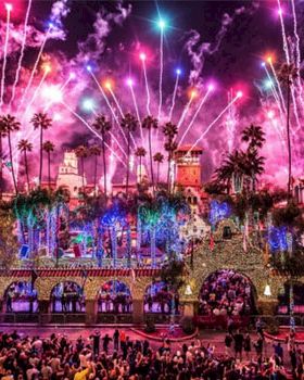 Colorful fireworks burst over a palm-lined town as crowds watch a festive celebration.