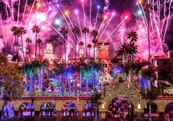 Colorful fireworks burst over a palm-lined town as crowds watch a festive celebration.