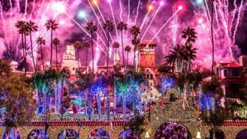Colorful fireworks burst over a palm-lined town as crowds watch a festive celebration.