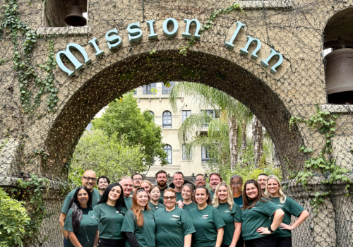 A group of people stands in front of the &ldquo;ADision 1&rdquo; archway at an old building.