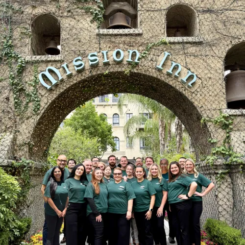 A group of people stands in front of the &ldquo;ADision 1&rdquo; archway at an old building.