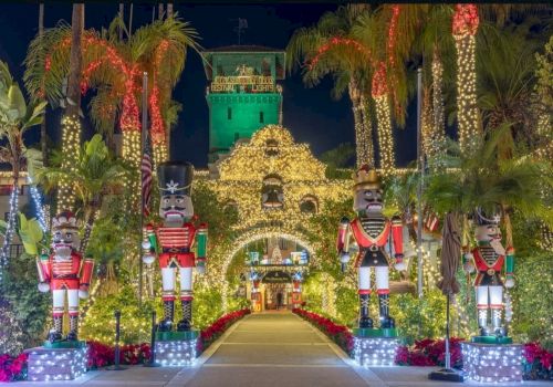 A festive holiday display with towering nutcracker figures, palm trees, and sparkling lights at a lit festival entrance.