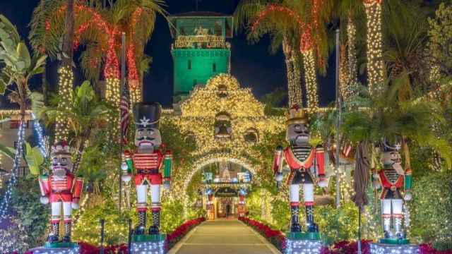 A festive holiday display with towering nutcracker figures, palm trees, and sparkling lights at a lit festival entrance.